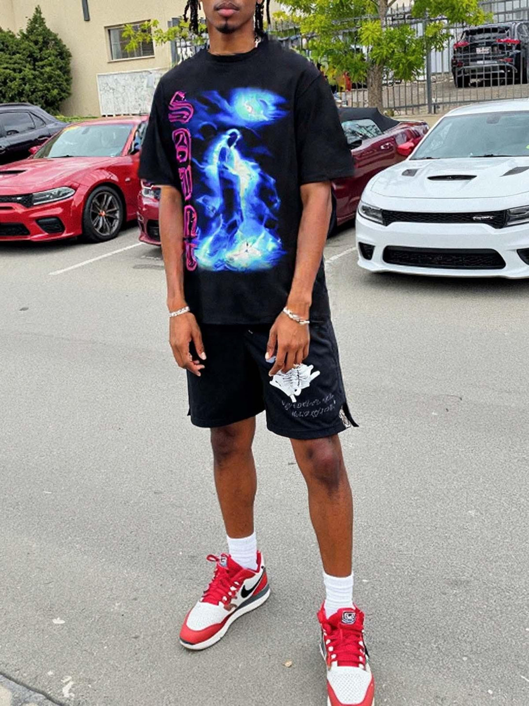 Model wearing TALISHKO "SAINT" graphic T-shirt with vibrant blue design, paired with red sneakers.