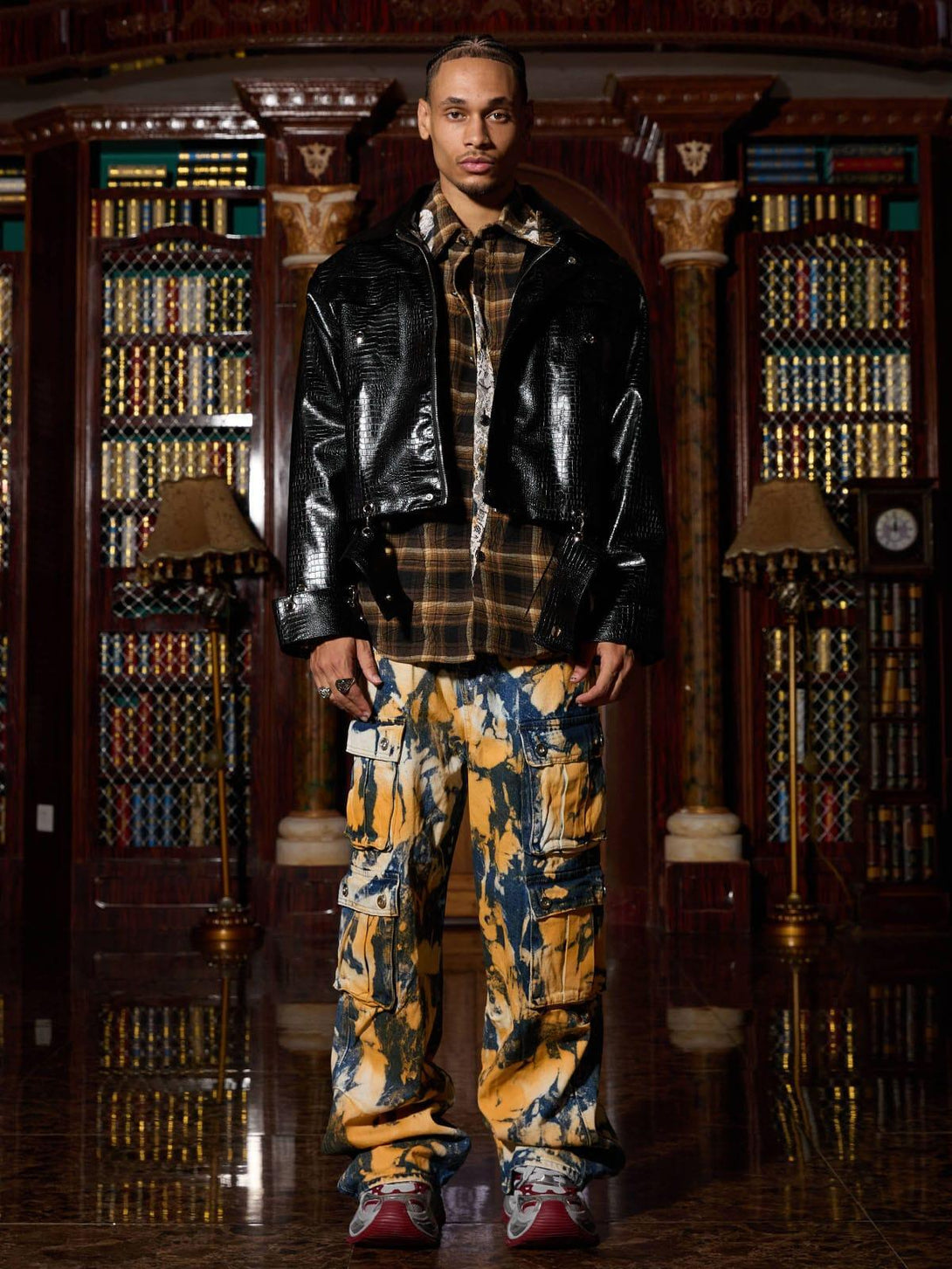 Model wearing TALISHKO's leather jacket with plaid shirt and vibrant cargo pants, stylishly edgy.