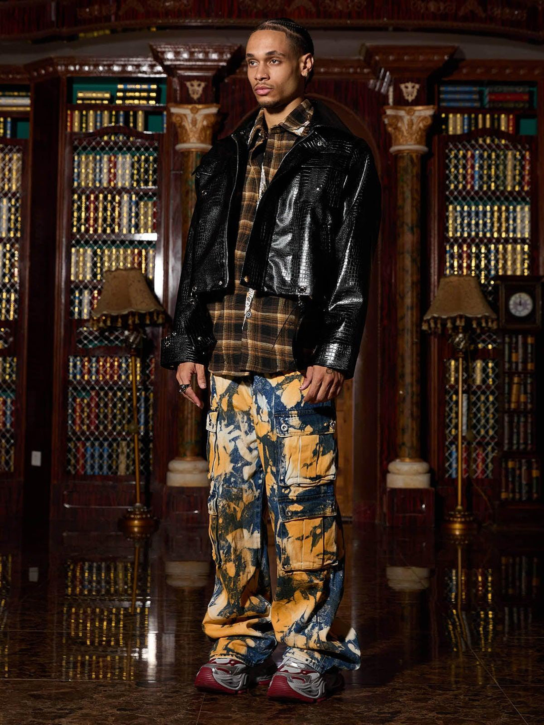 Model in TALISHKO's leather jacket, plaid shirt, and colorful cargo pants, library backdrop.