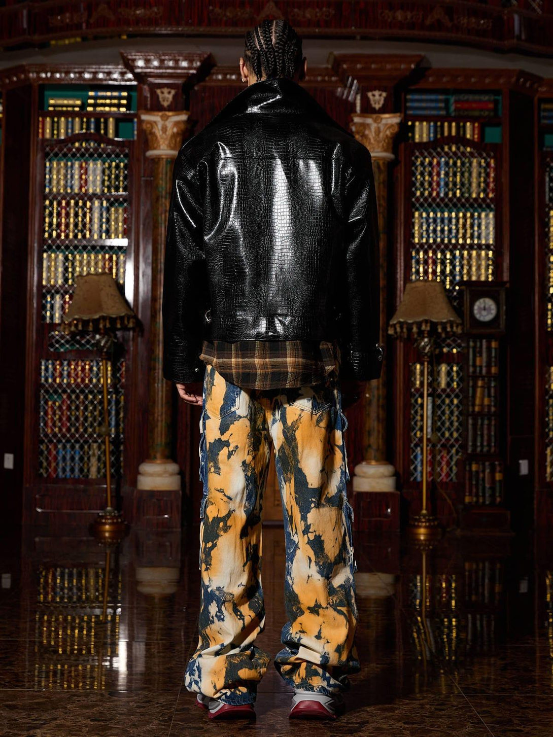 Back view of TALISHKO's textured leather jacket paired with bold cargo pants in a library setting.