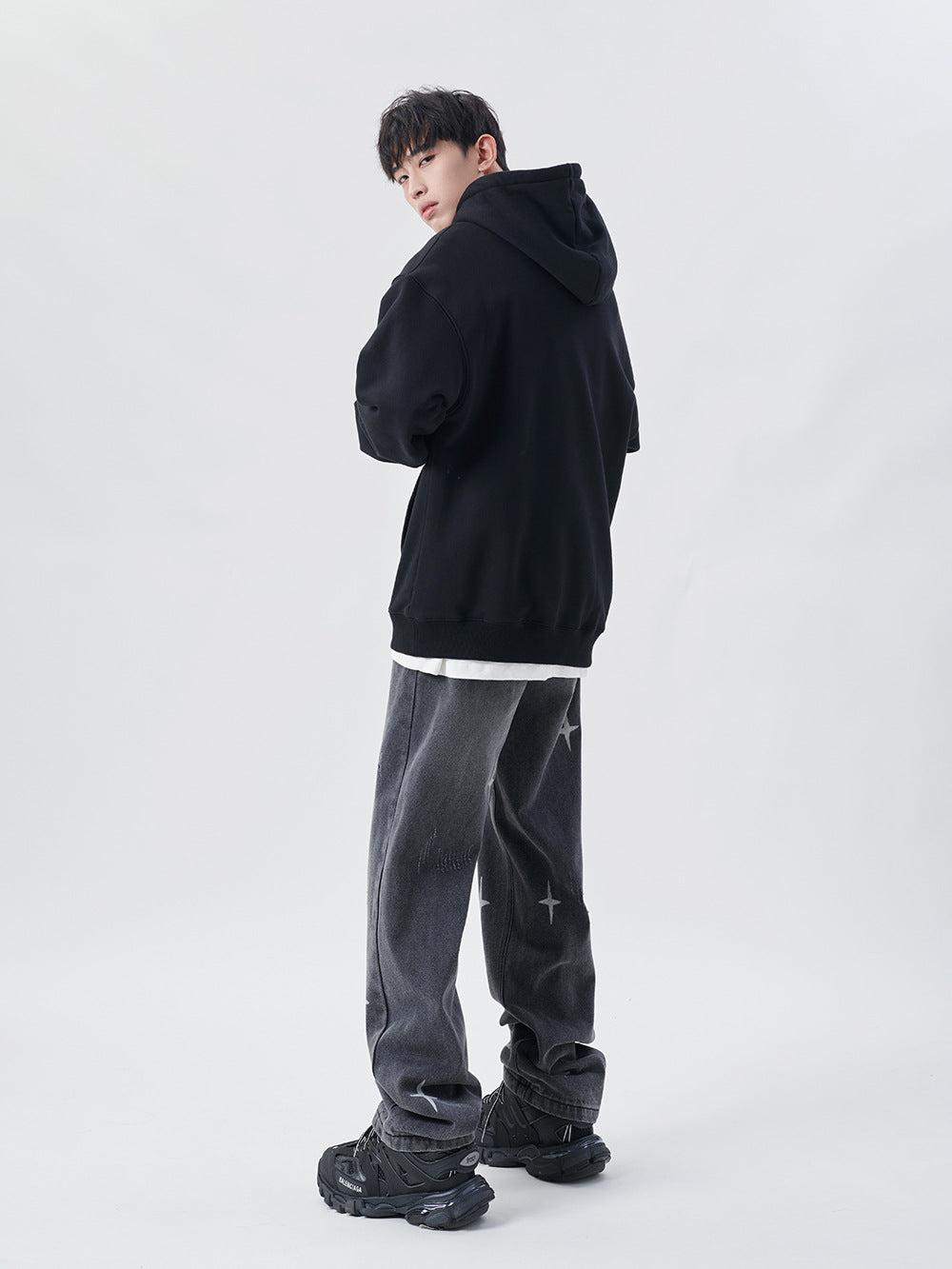 Model in TALISHKO black hoodie and gray jeans with star details, embodying streetwear style.
