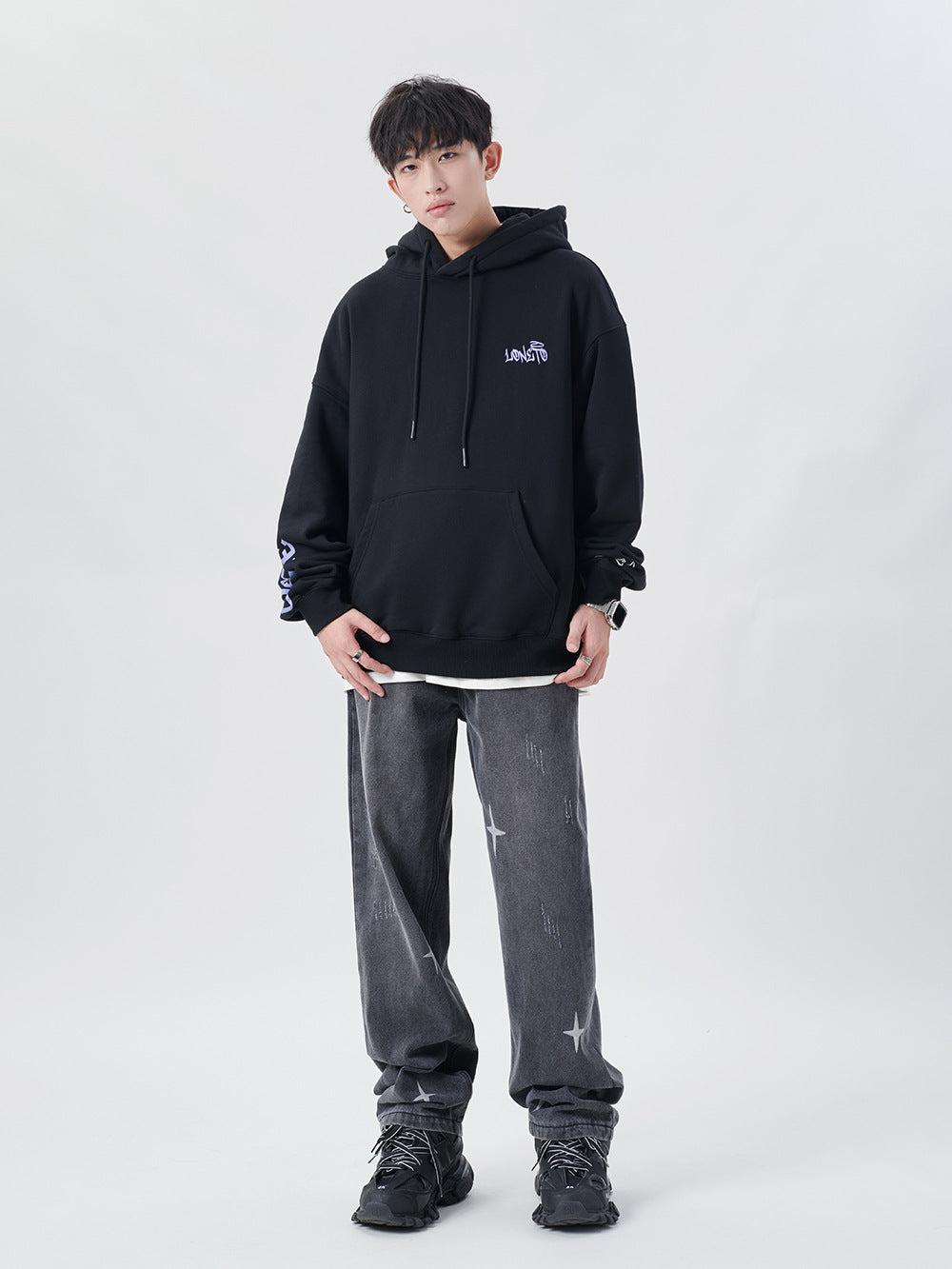 Model wearing TALISHKO black hoodie and gray shredded jeans with star details, showcasing casual style.