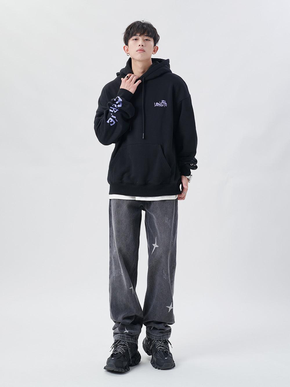 Model in TALISHKO black hoodie and gray star-patterned jeans, highlighting urban fashion style.