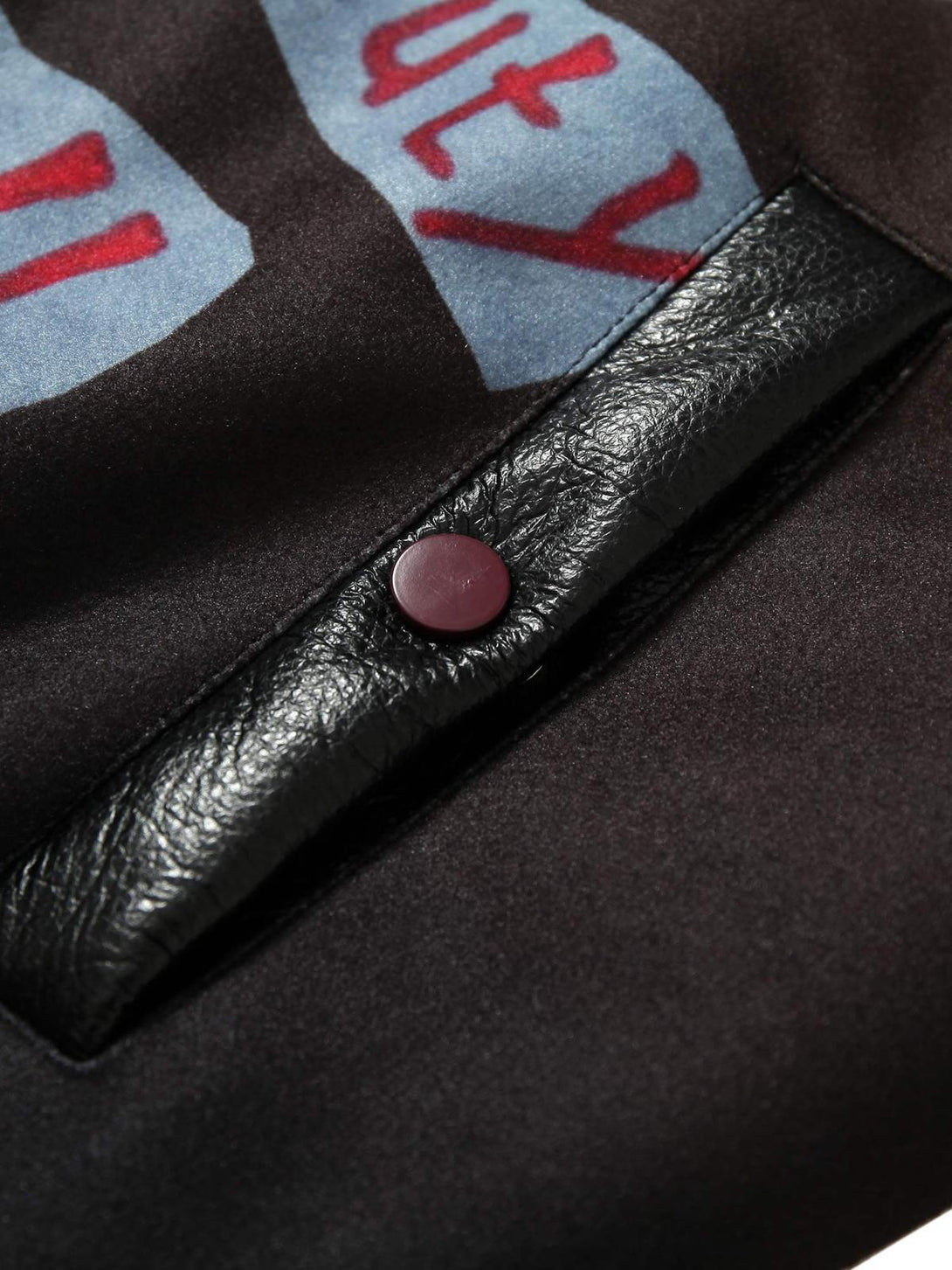 A close-up of the TALISHKO bomber jacket's leather button detail and embroidery texture.