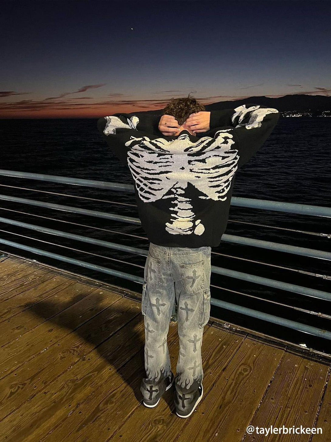 Back view of TALISHKO's skeleton knit sweater paired with cross-patterned jeans at sunset.