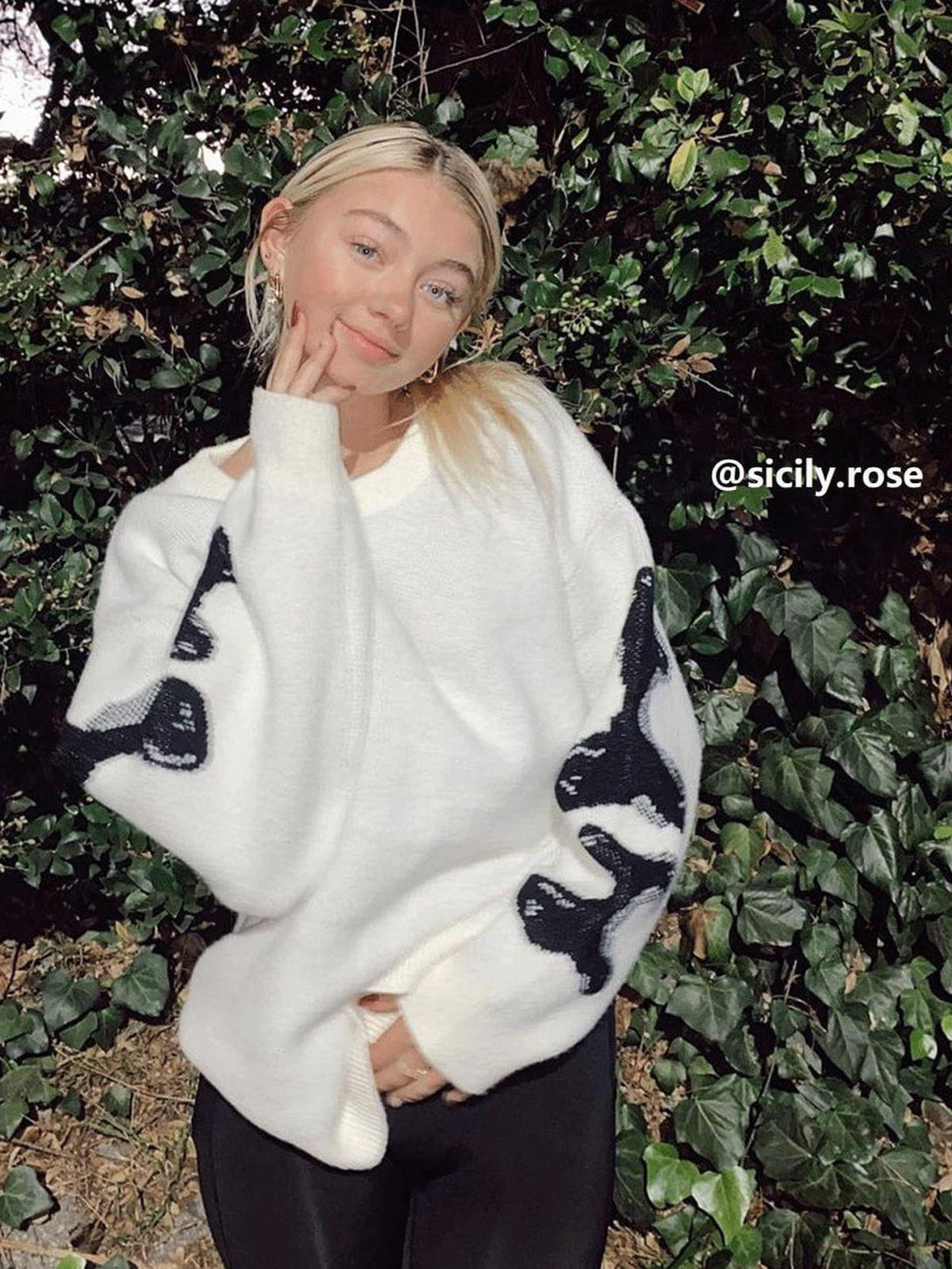 Person poses in a white TALISHKO skeleton pattern knit sweater amidst lush greenery.