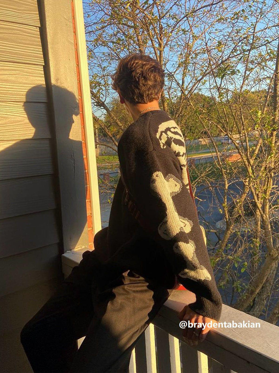 Person wearing TALISHKO's skeleton pattern knit sweater, enjoying a sunny outdoor view.