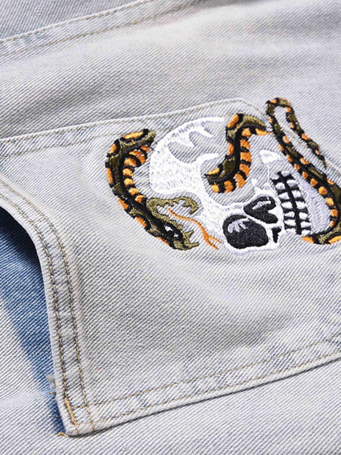 Intricate look at TALISHKO embroidered jeans, featuring a skull and snake design on light denim.