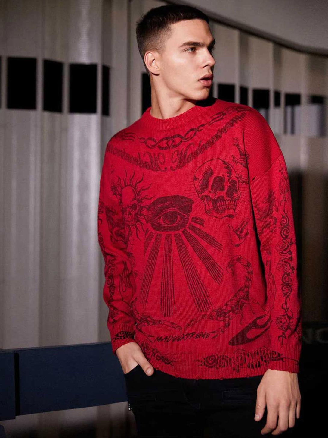 Model in a red TALISHKO sweater featuring intricate skull and eye designs, creating an edgy look.