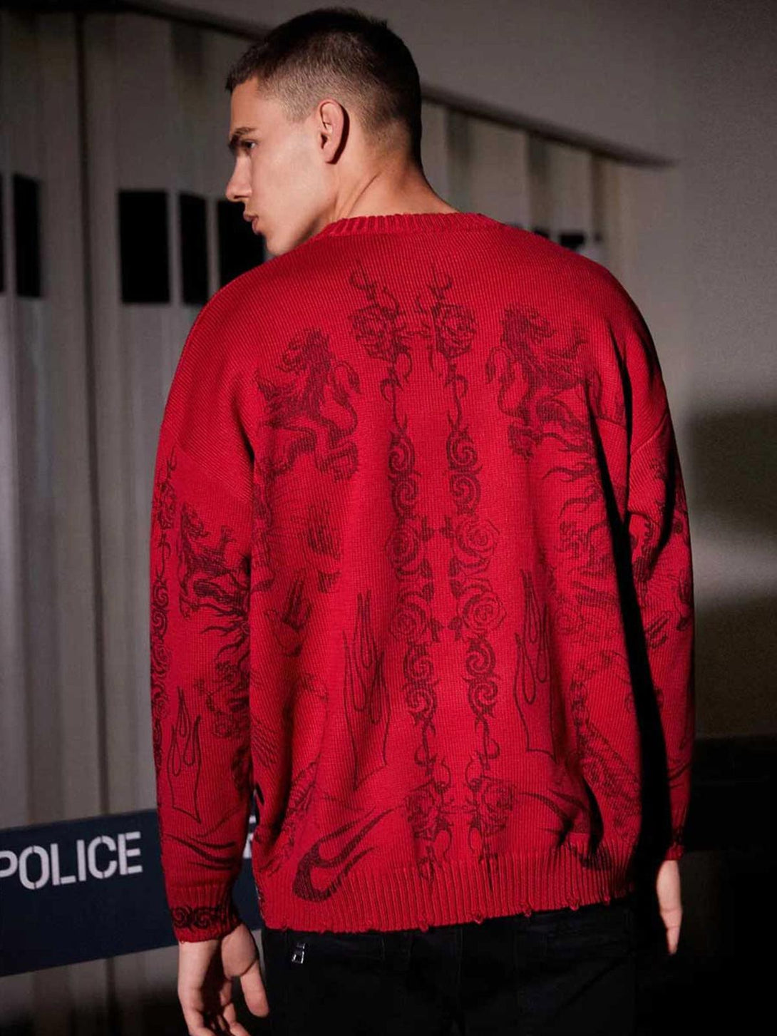 Model showcasing a red TALISHKO sweater with intricate designs, emphasizing bold street style.