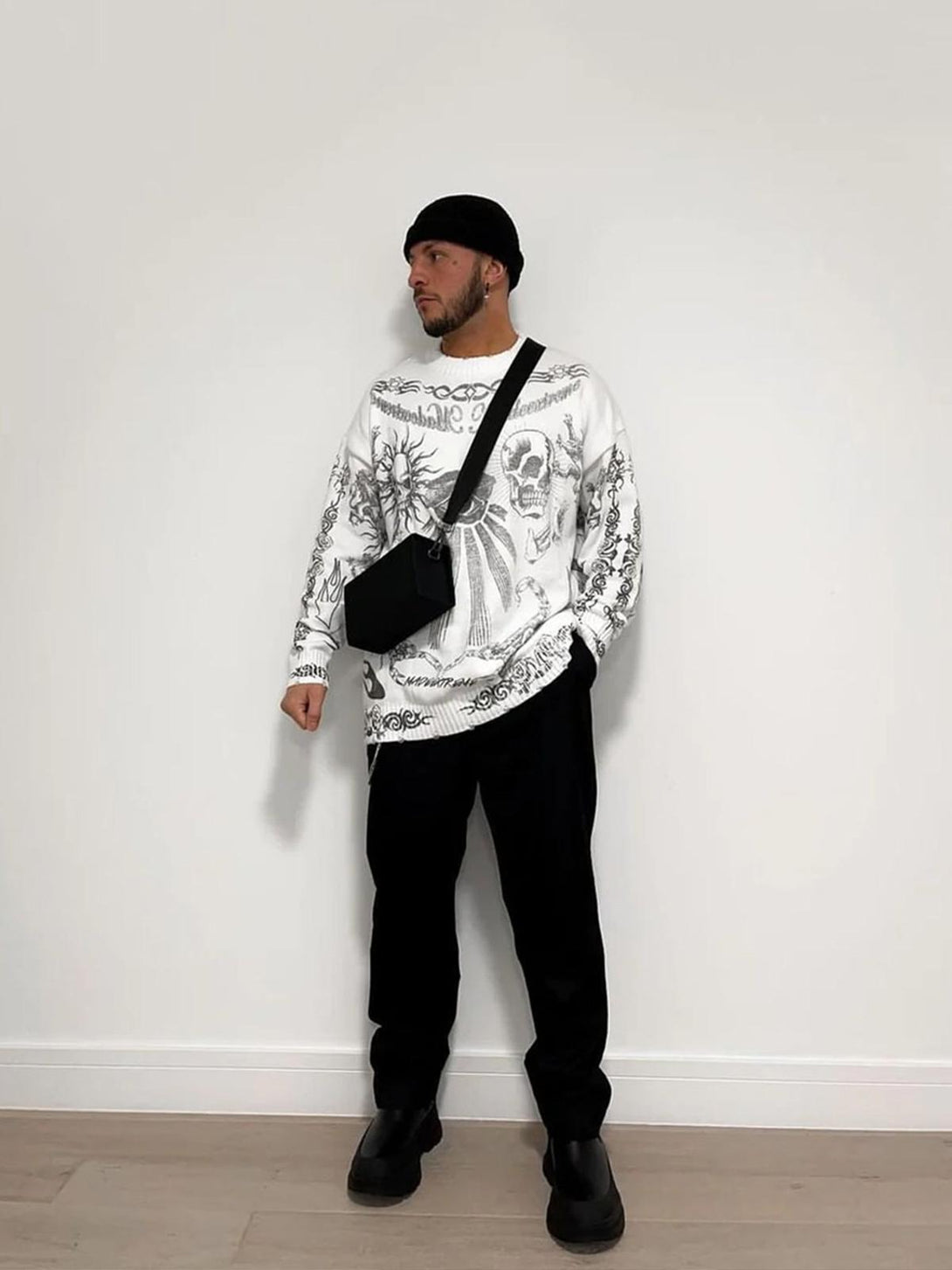 Model wearing a TALISHKO skull print distressed sweater with black pants and a crossbody bag.
