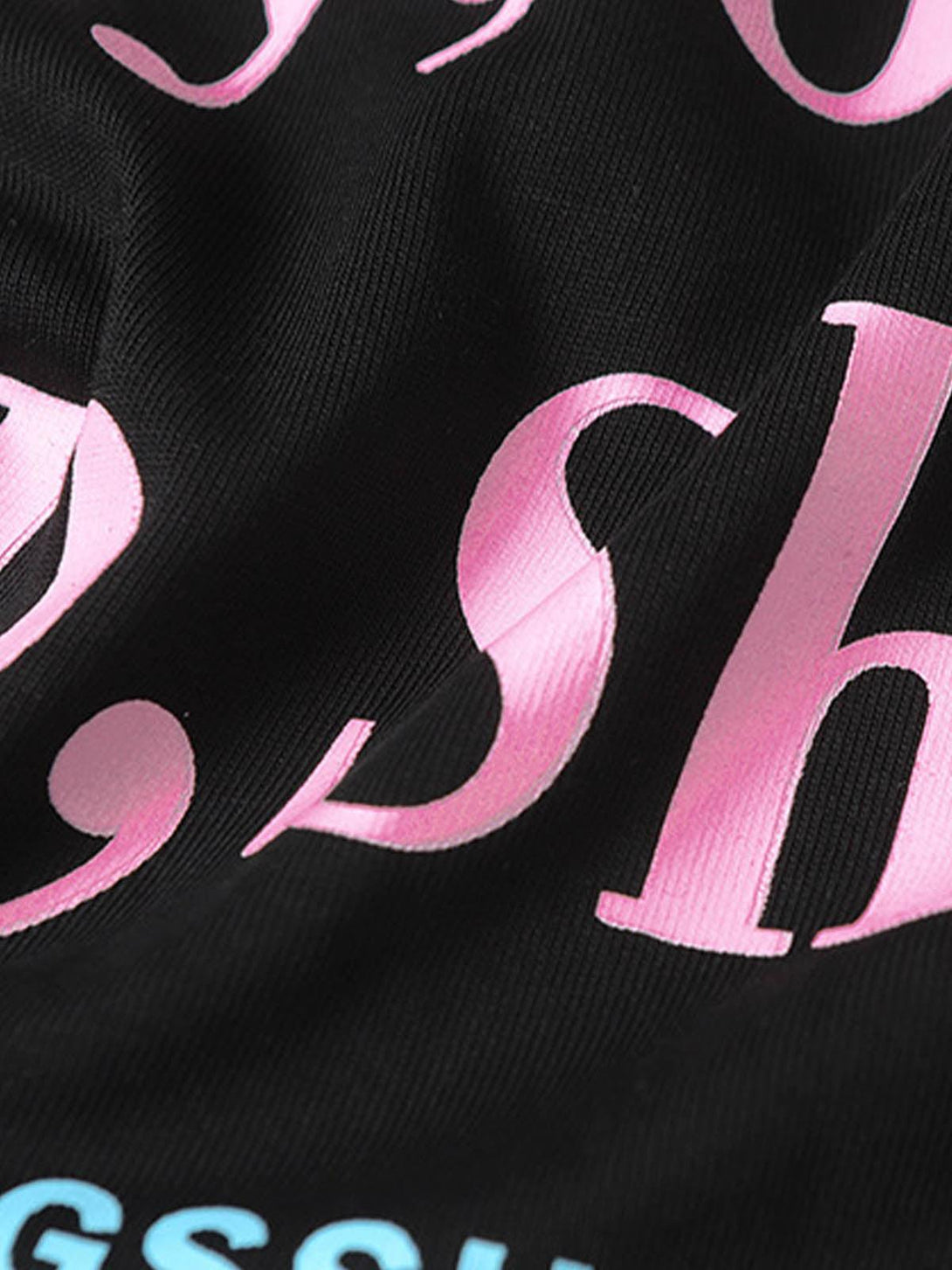 A close-up of pink and blue text on a black TALISHKO slogan graphic T-shirt, highlighting design details.