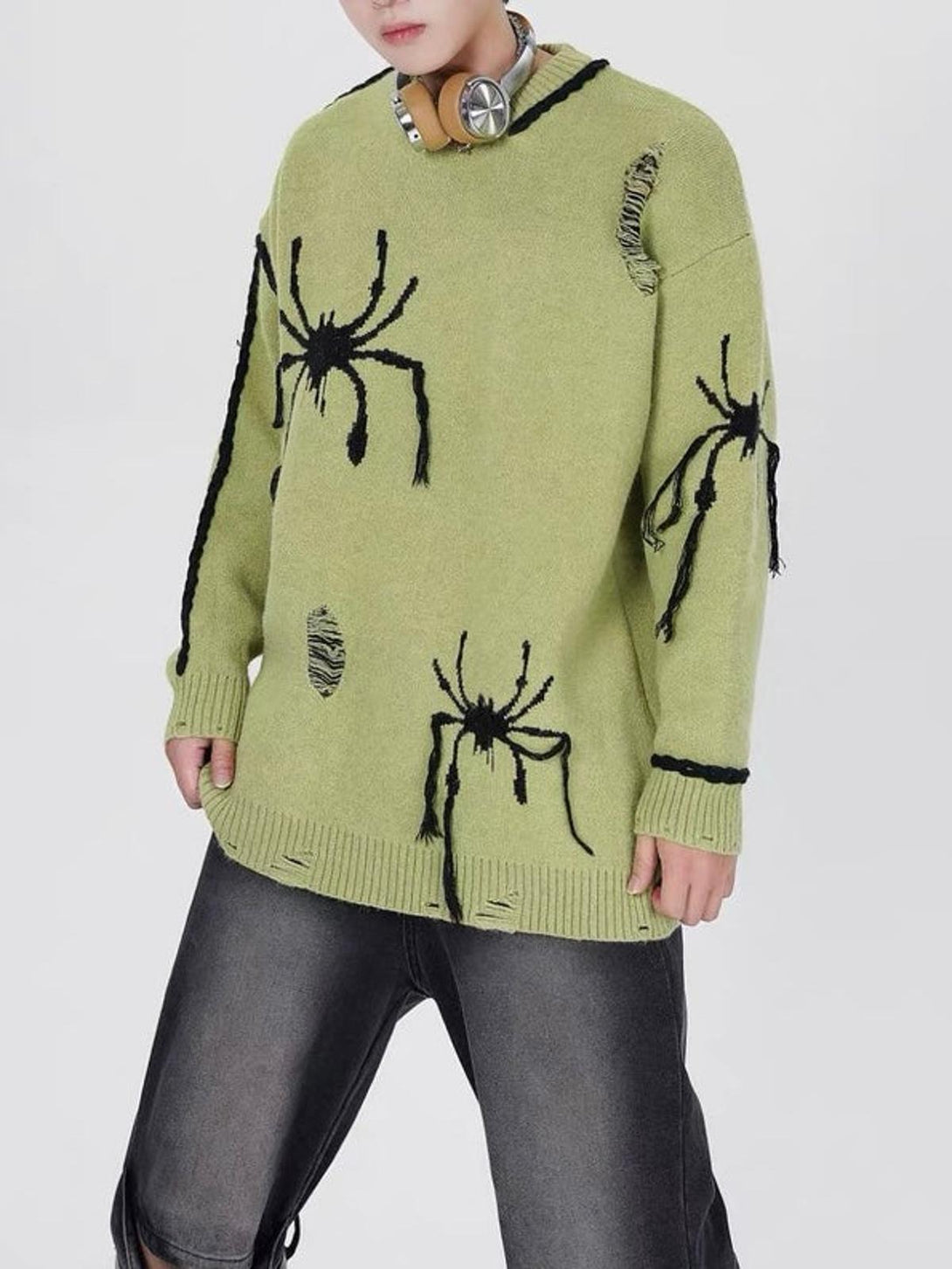 Model wearing a green oversized sweater with spider motifs and distressed accents by TALISHKO.