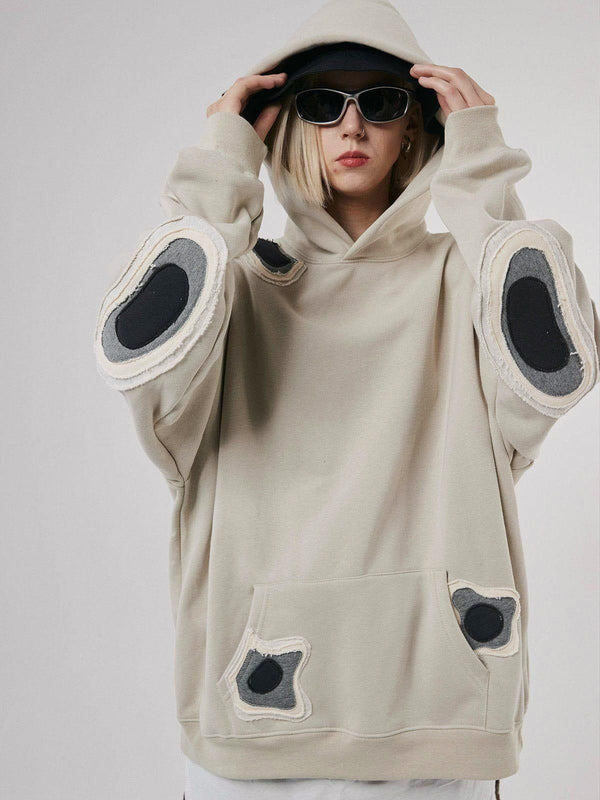 Model wearing a TALISHKO spot patchwork hoodie, featuring unique circular patches on the sleeves.