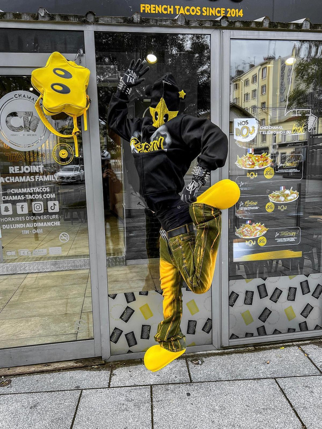 Person in TALISHKO star-embroidered hoodie and yellow accents, striking a playful pose.