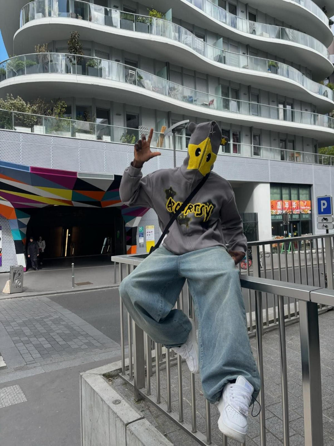 Person wearing TALISHKO star-embroidered hoodie, sitting on a railing in an urban setting.