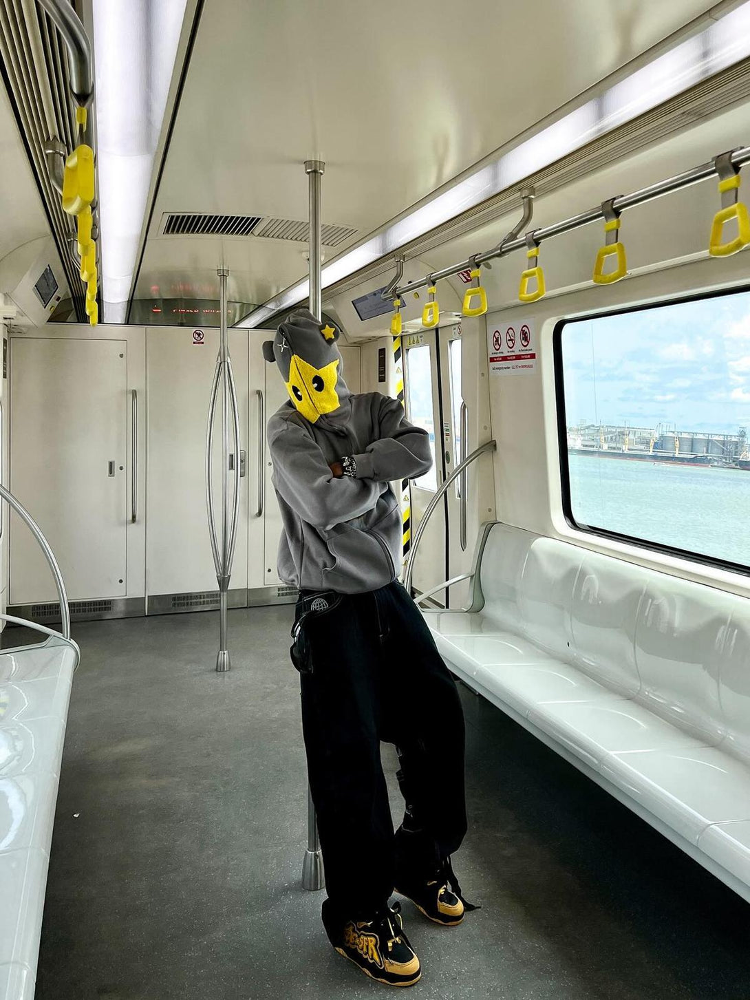 Person in TALISHKO hooded sweatshirt with yellow star detail, posing confidently in a train.