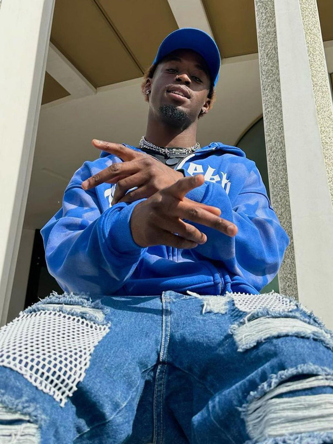 Model wearing a blue TALISHKO hoodie with star print and distressed jeans, capturing streetwear style.