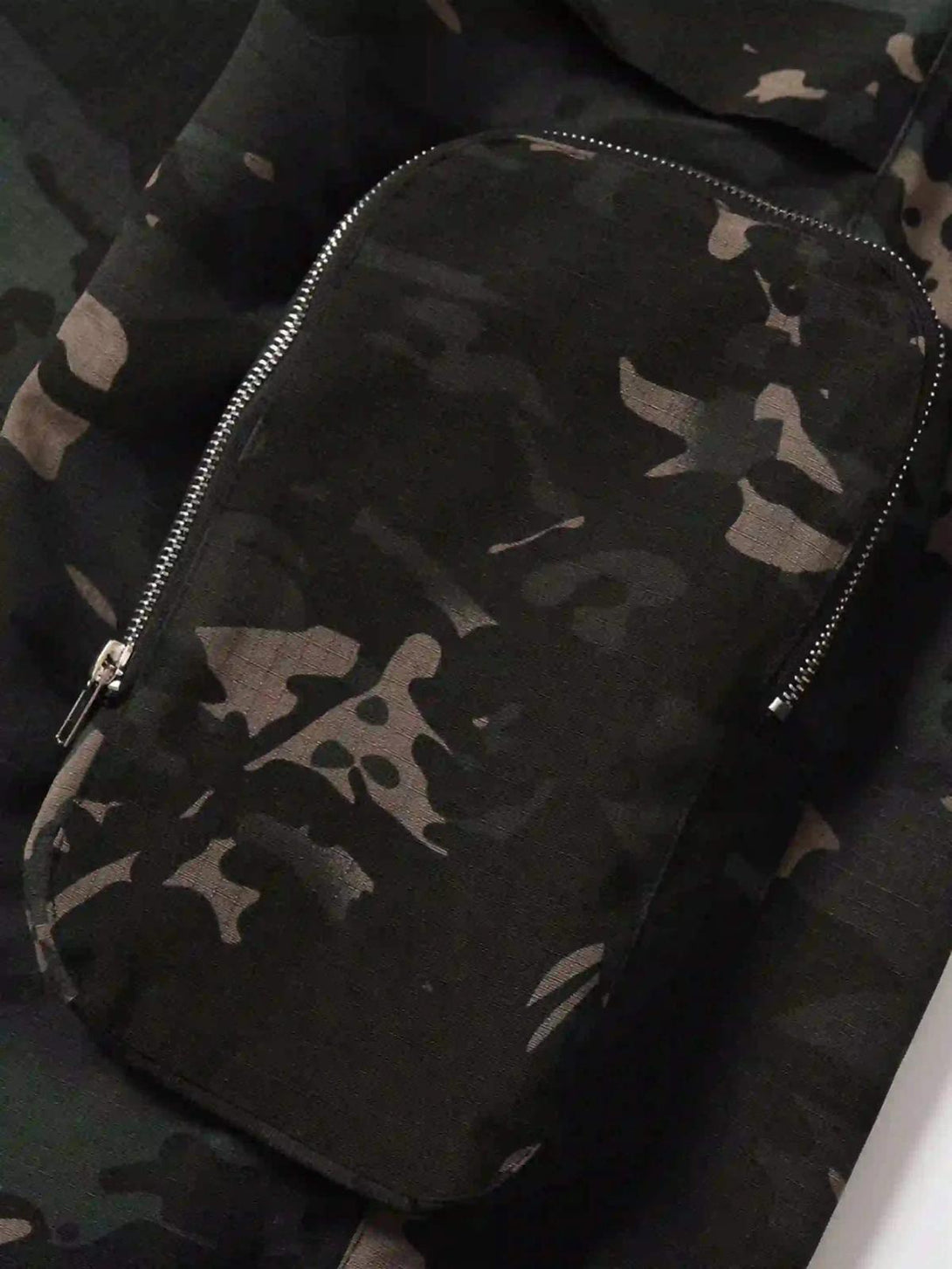 A detailed view of TALISHKO cargo pants highlighting the camouflage pattern and zipper detail.