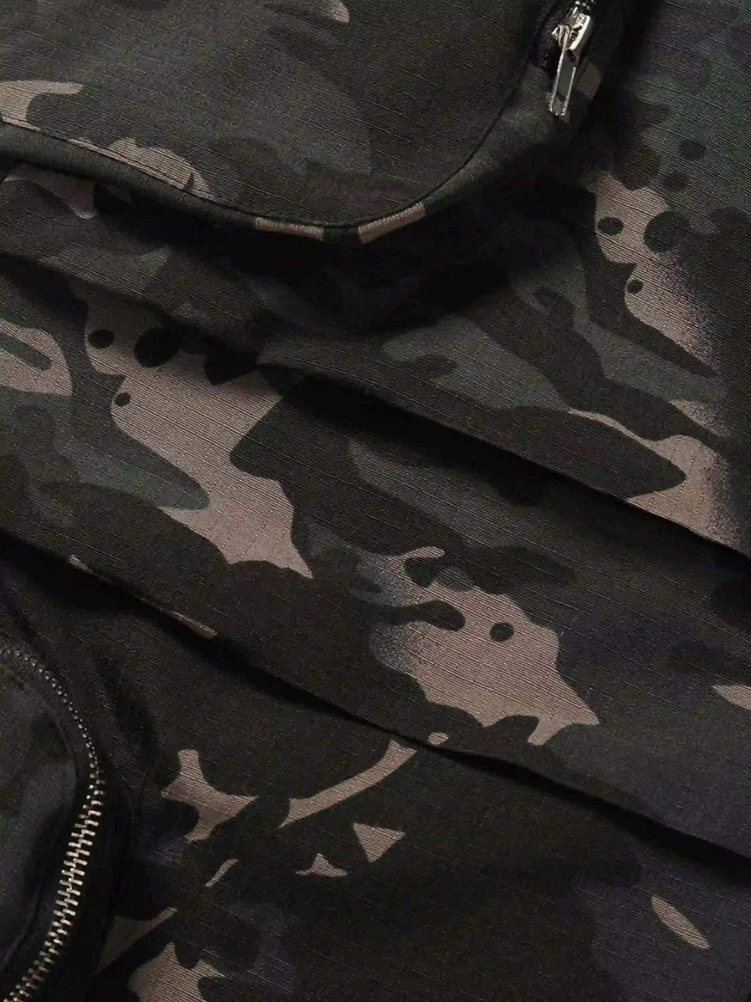 A close-up of TALISHKO's dark camouflage cargo pants, highlighting sleek zipper details.