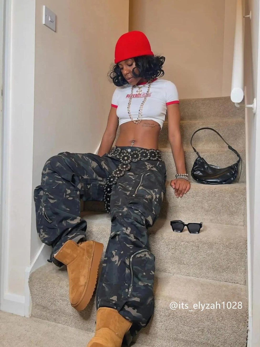 Model showcasing TALISHKO street-style cargo pants with bold zippers and a chic red hat.