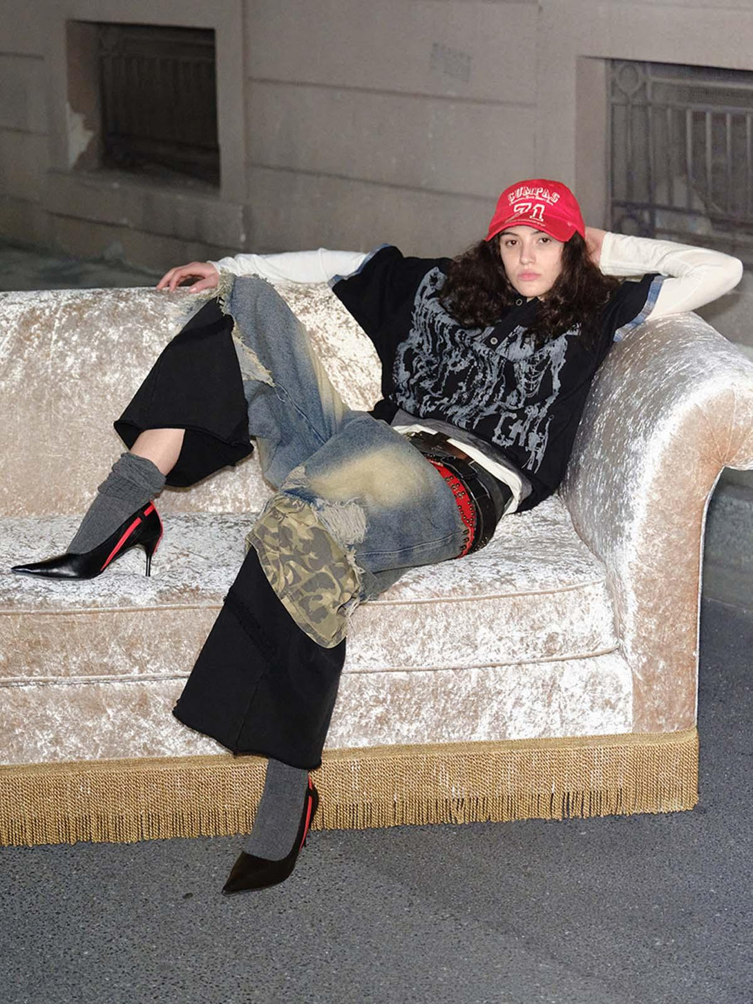 Model reclining in an urban setting, wearing TALISHKO graffiti polo shirt and layered streetwear.