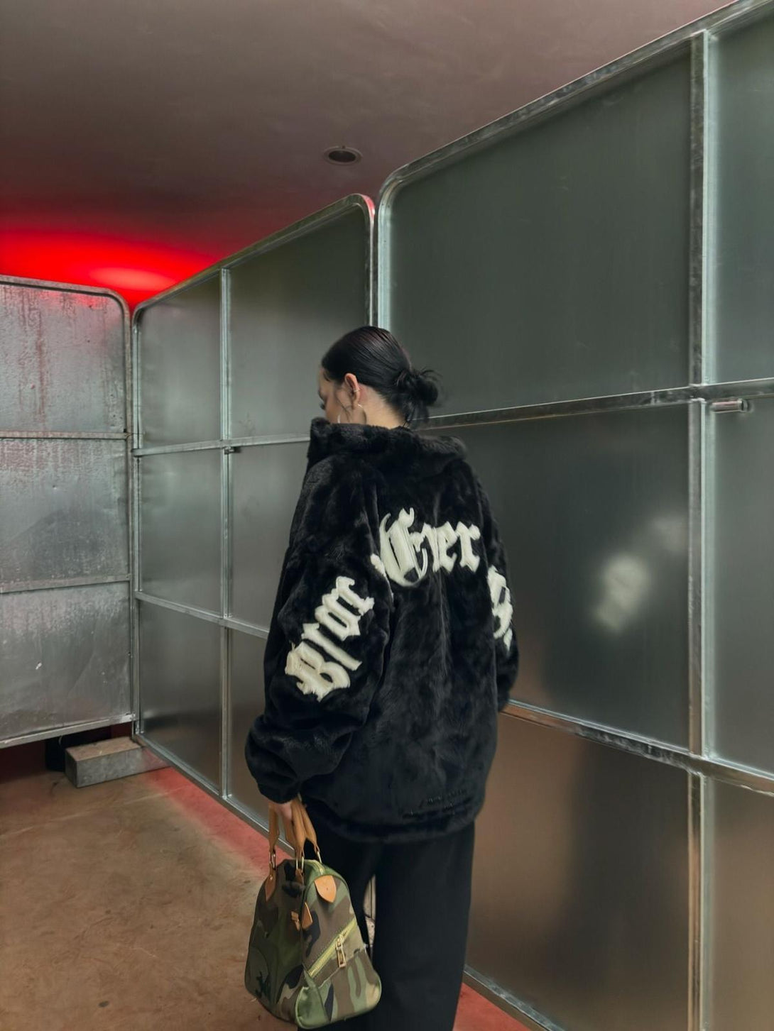Back view of TALISHKO fleece jacket with street-style embroidery, paired with a camo bag.