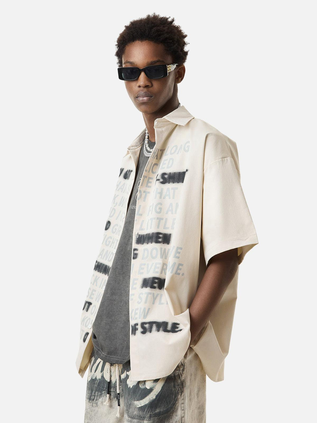 Model in TALISHKO short sleeve shirt with letter print, styled with sunglasses and layered chains.