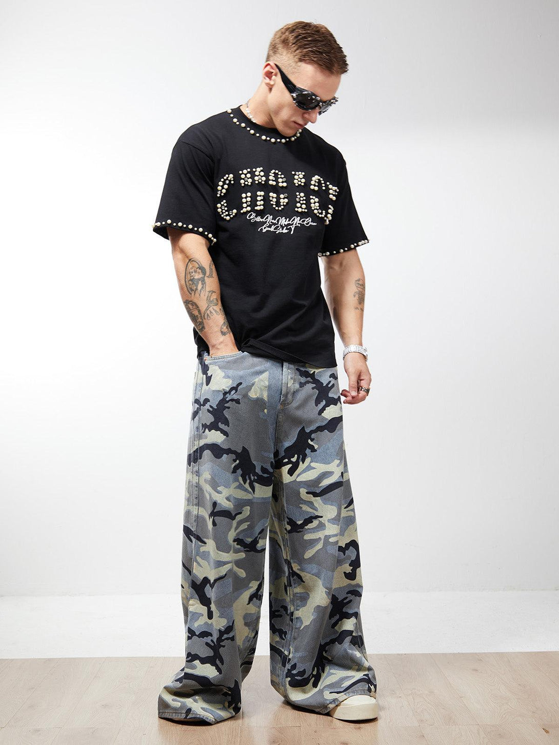 Model wearing TALISHKO black studded tee and camouflage baggy jeans for a bold streetwear look.