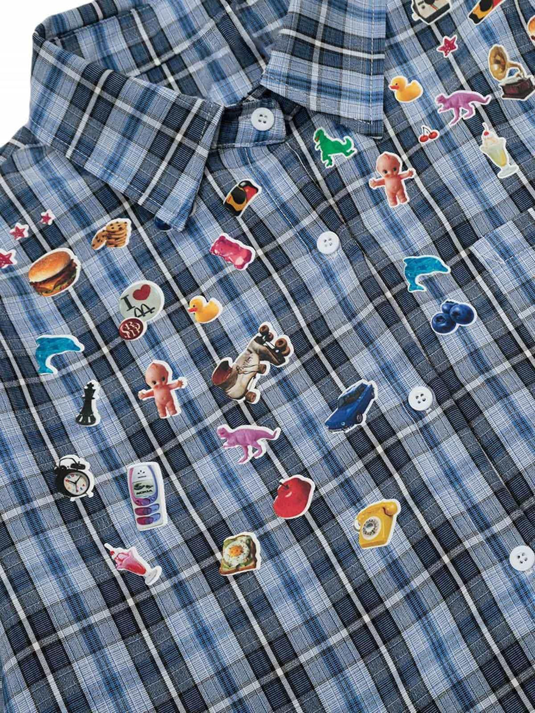 A close-up of TALISHKO's plaid shirt adorned with whimsical stickers on a blue checkered pattern.