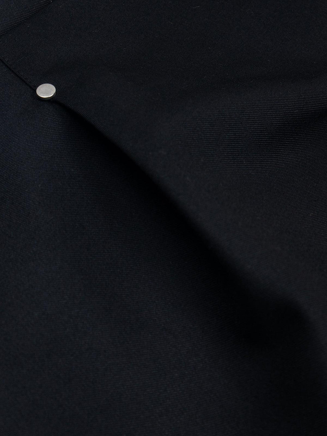 A tight crop highlighting the rivet detail on TALISHKO's retro pleated shorts in dark fabric.
