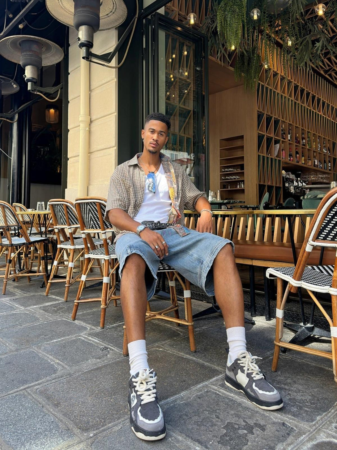 Model in a TALISHKO short-sleeved shirt and denim shorts, seated casually outside a café.
