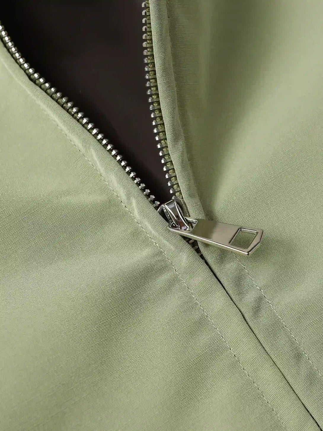 Focusing on the zip detail of TALISHKO's green jacket, showcasing sleek streetwear style.