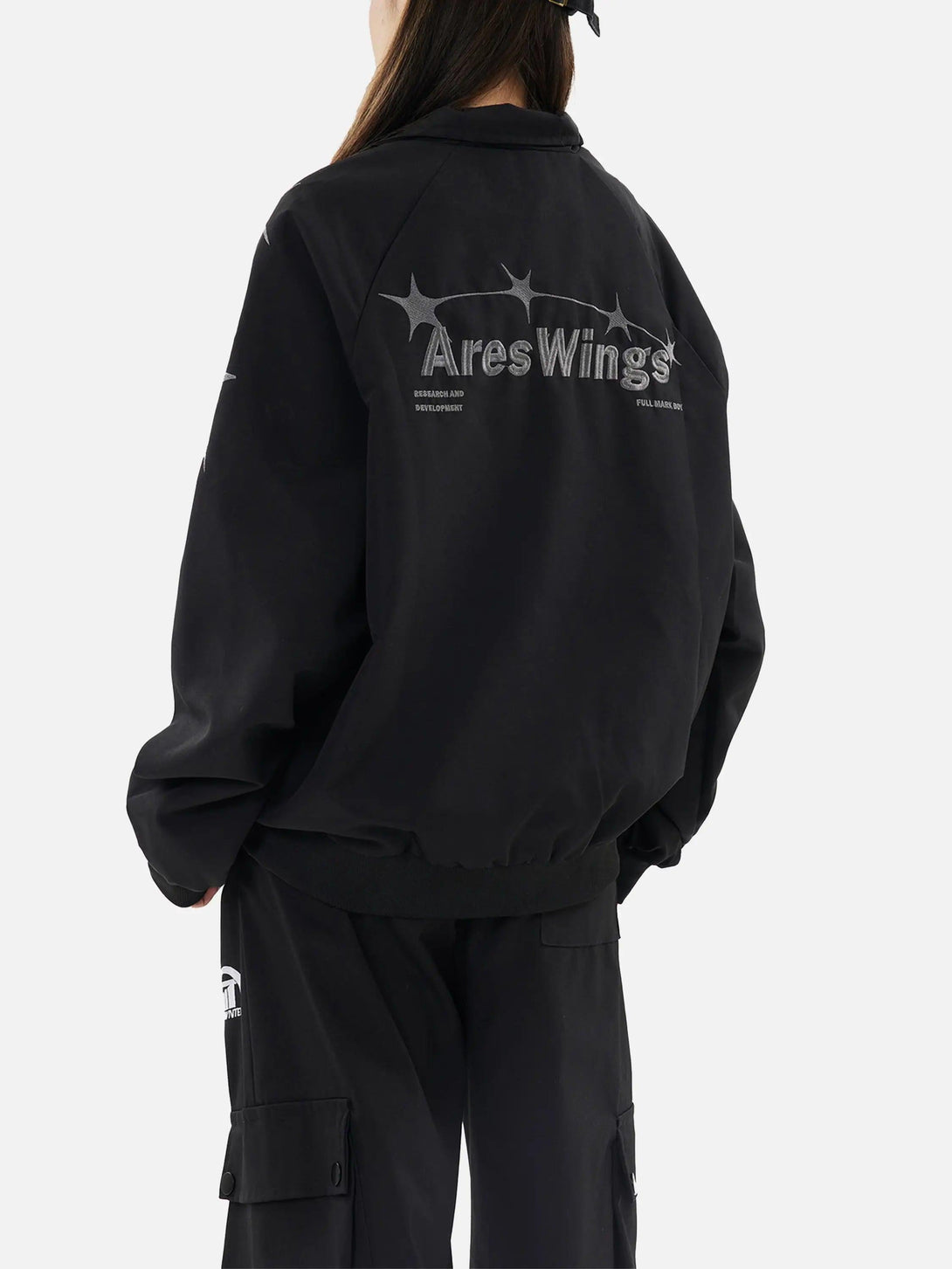 Model wearing TALISHKO's black zip-up jacket with star embroidery, back view emphasizing street style.