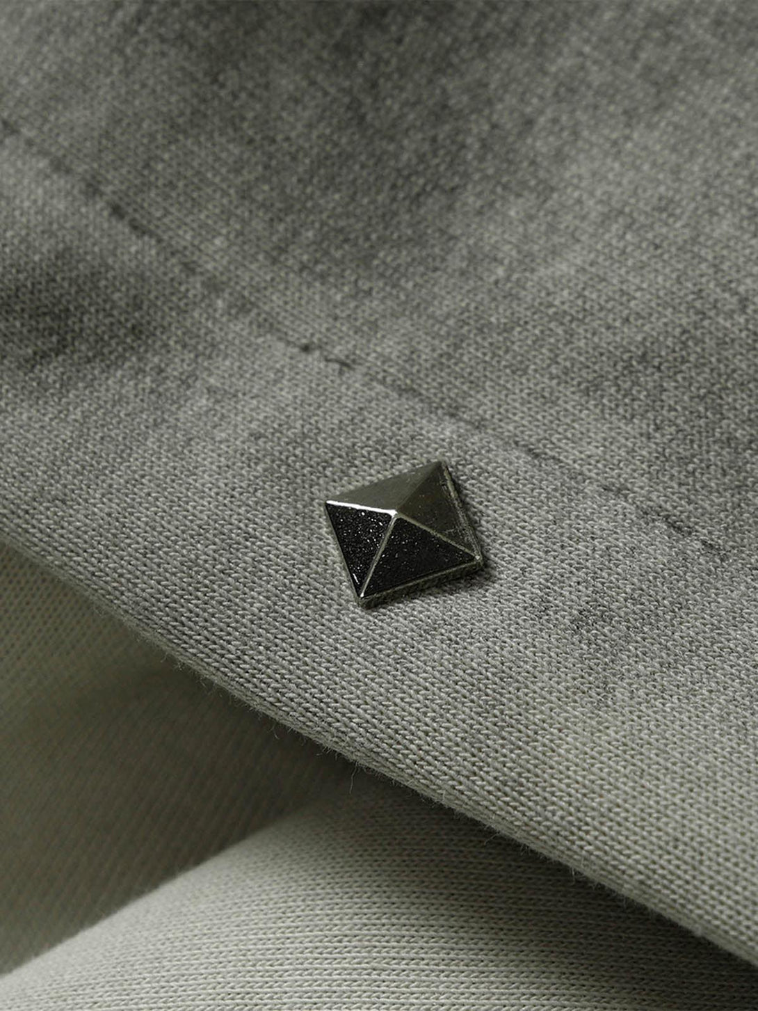 Zoomed-in texture of a TALISHKO jacket, focusing on rivet detail and fabric stitching.