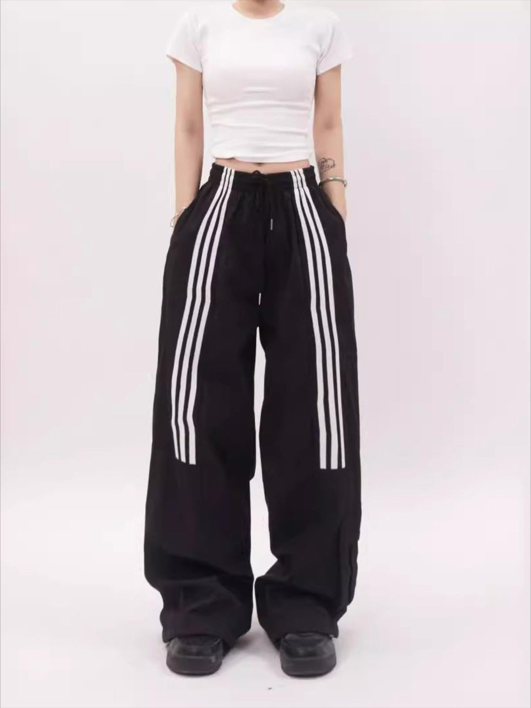 Model wearing black striped draped sweatpants by TALISHKO, showcasing a relaxed, casual fit.
