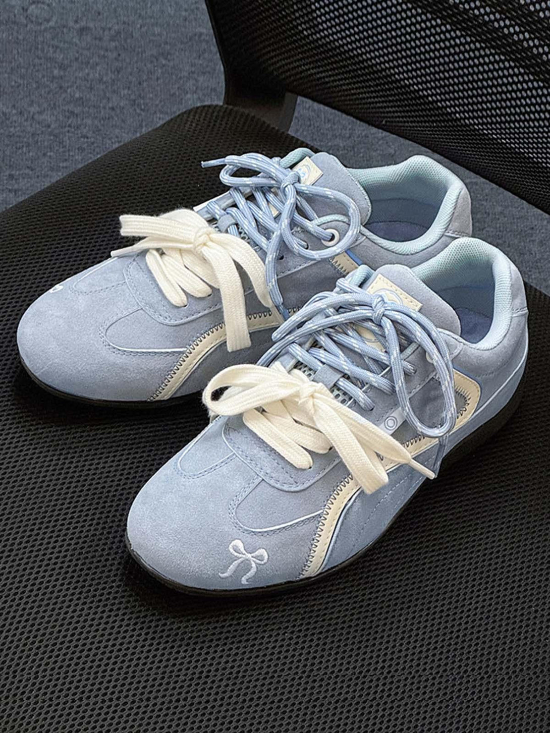 Light blue suede lace-up sneakers by TALISHKO on a mesh chair, featuring playful embroidery.