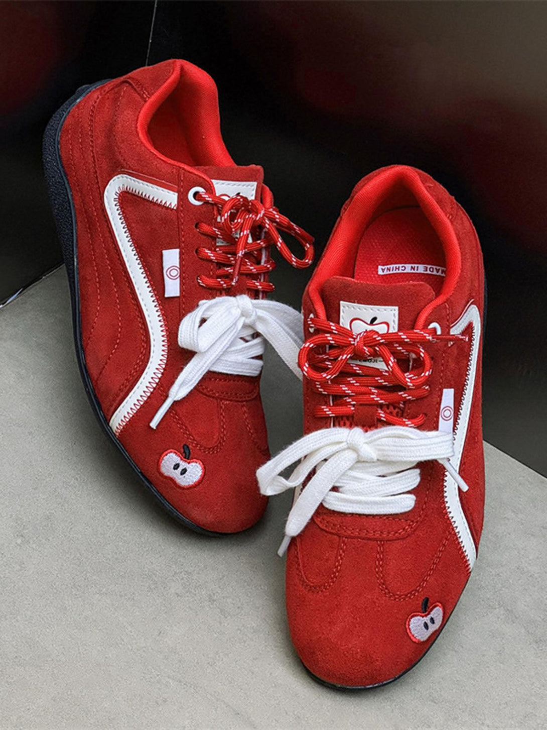Red suede lace-up sneakers by TALISHKO, featuring apple embroidery and vibrant design.