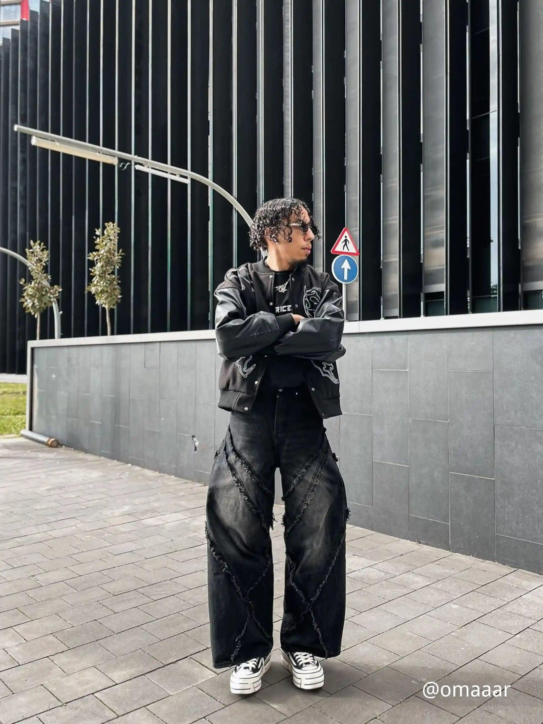 Model styled in TALISHKO's symbol-embroidered racing jacket, paired with wide-leg jeans and sneakers.