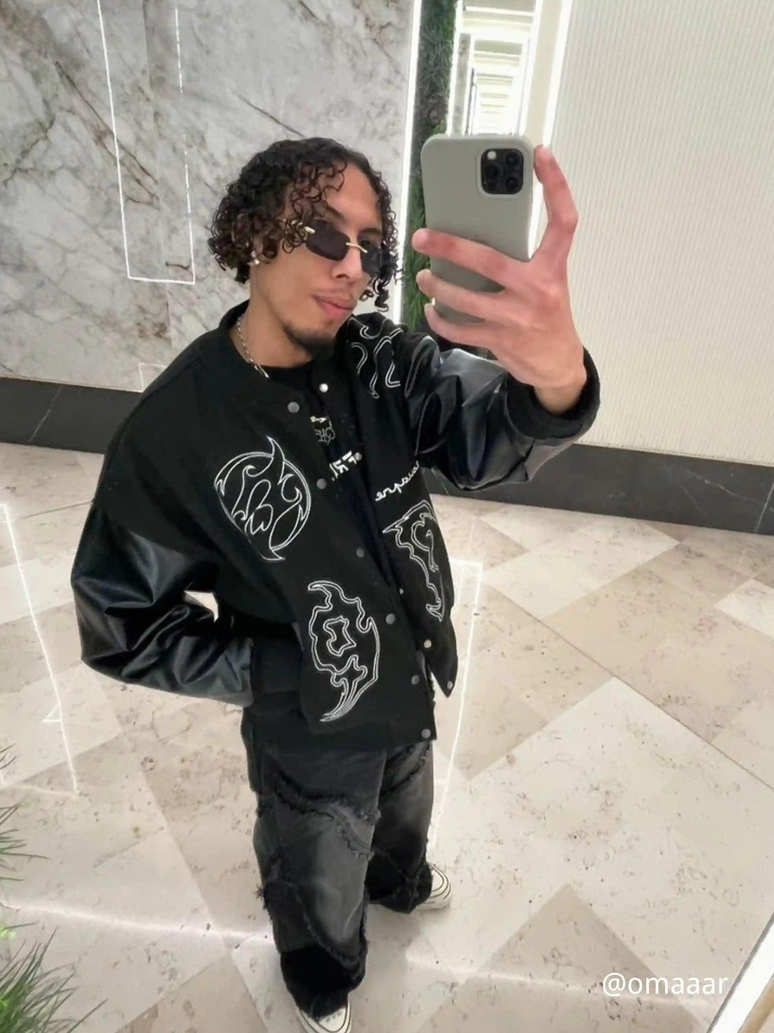 Model wearing TALISHKO's symbol-embroidered racing jacket with PU leather sleeves in a stylish setting.