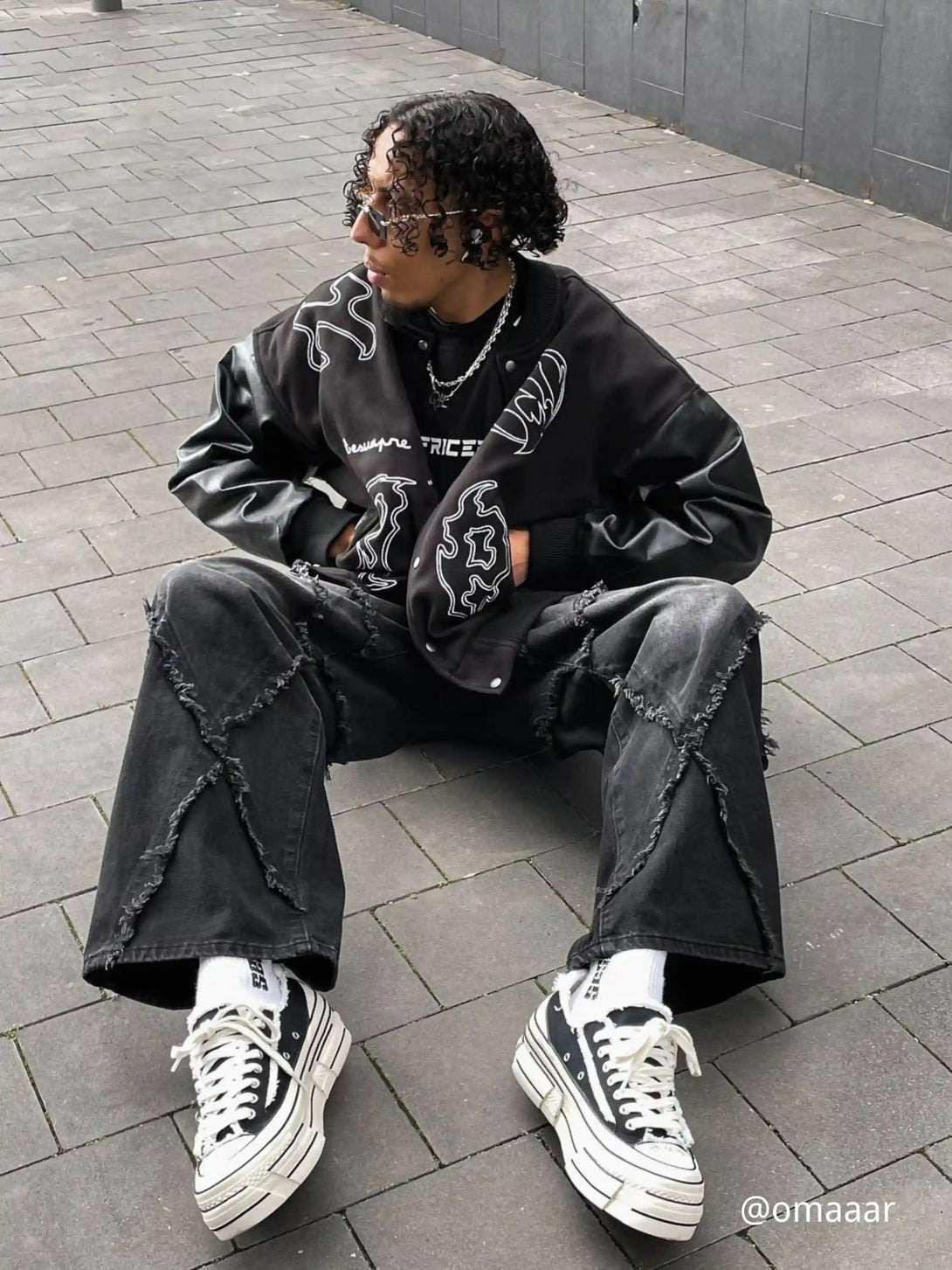 Model seated in TALISHKO's symbol-embroidered racing jacket, paired with edgy wide-leg jeans.