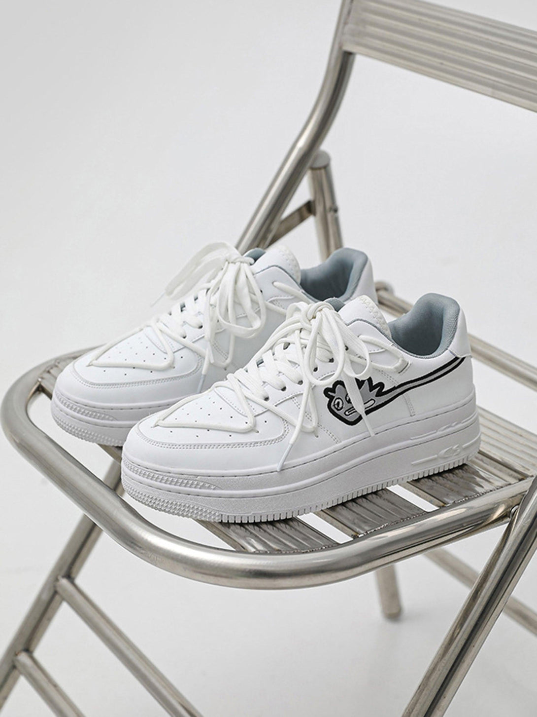 White TALISHKO sneakers with a playful monster design, front view on a metal chair.