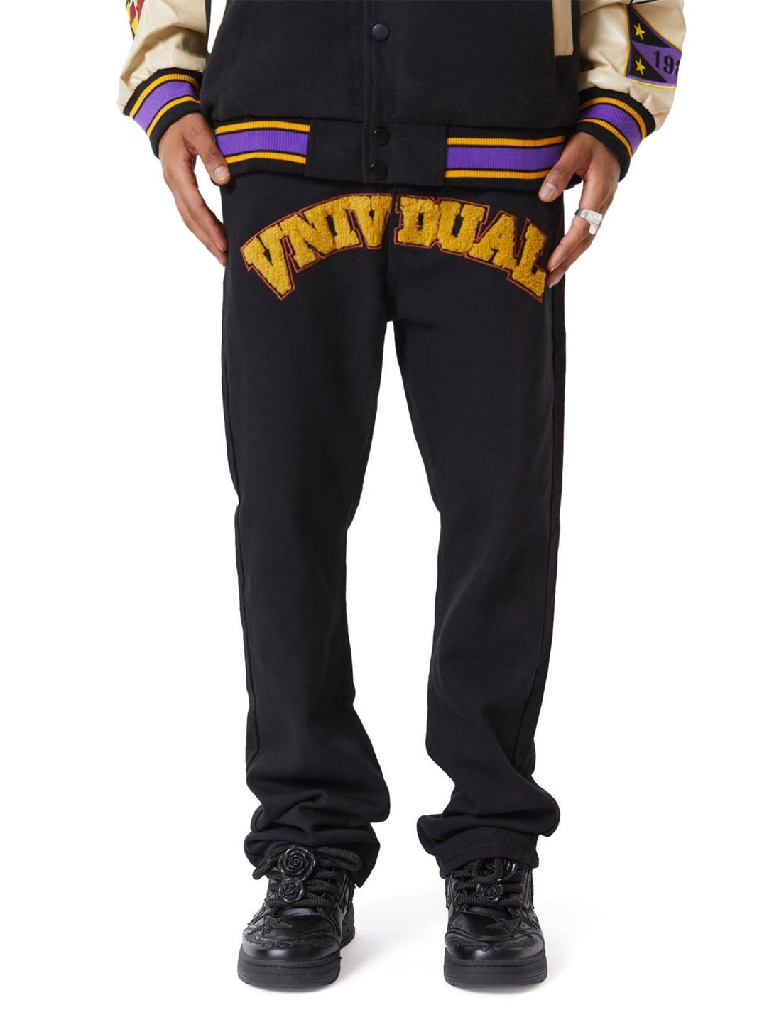 Model wearing TALISHKO jeans with bold yellow lettering, styled for a casual streetwear look.