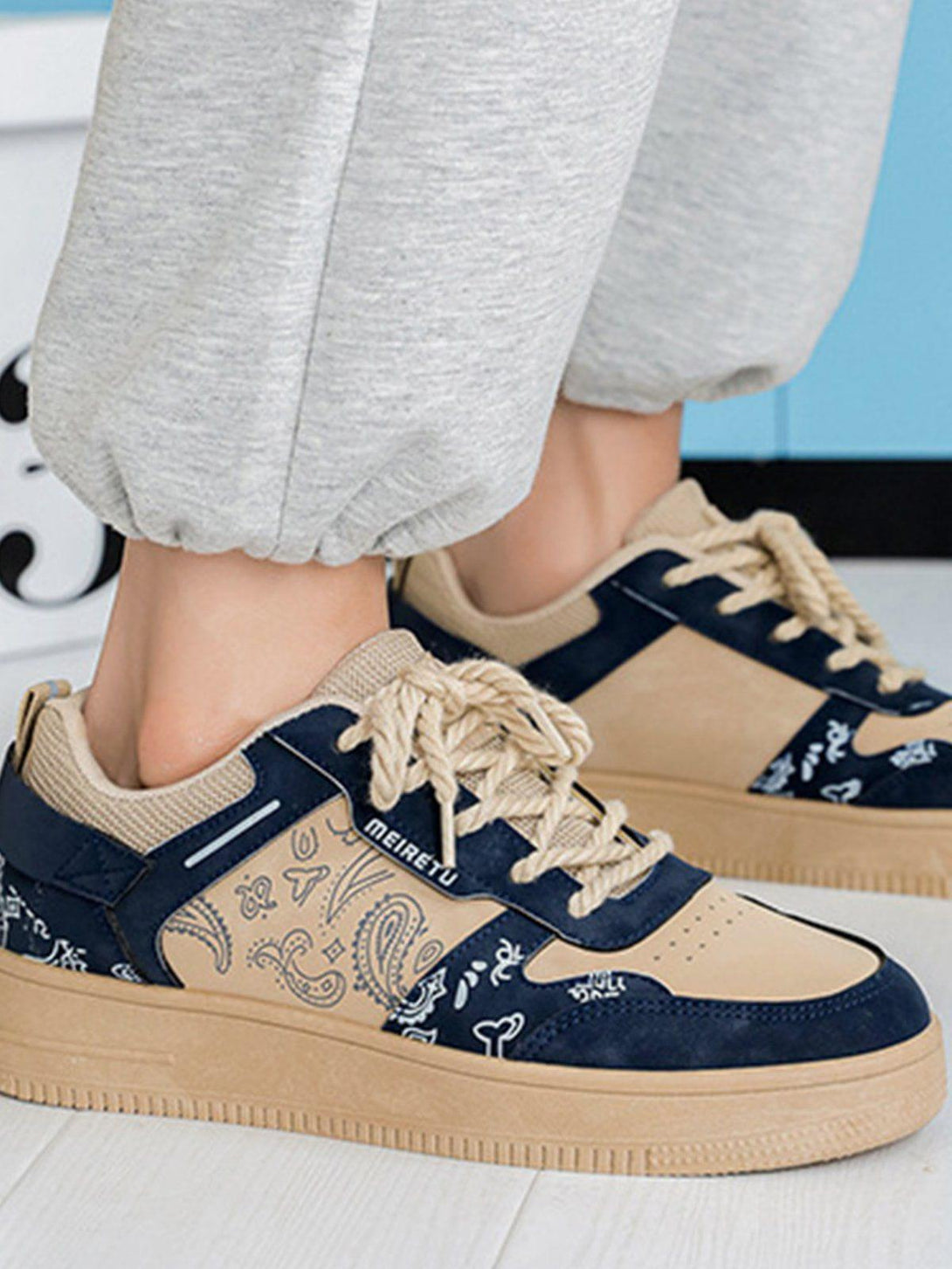 Front view of TALISHKO men's shoes in blue with cashew flower print, paired with gray joggers.