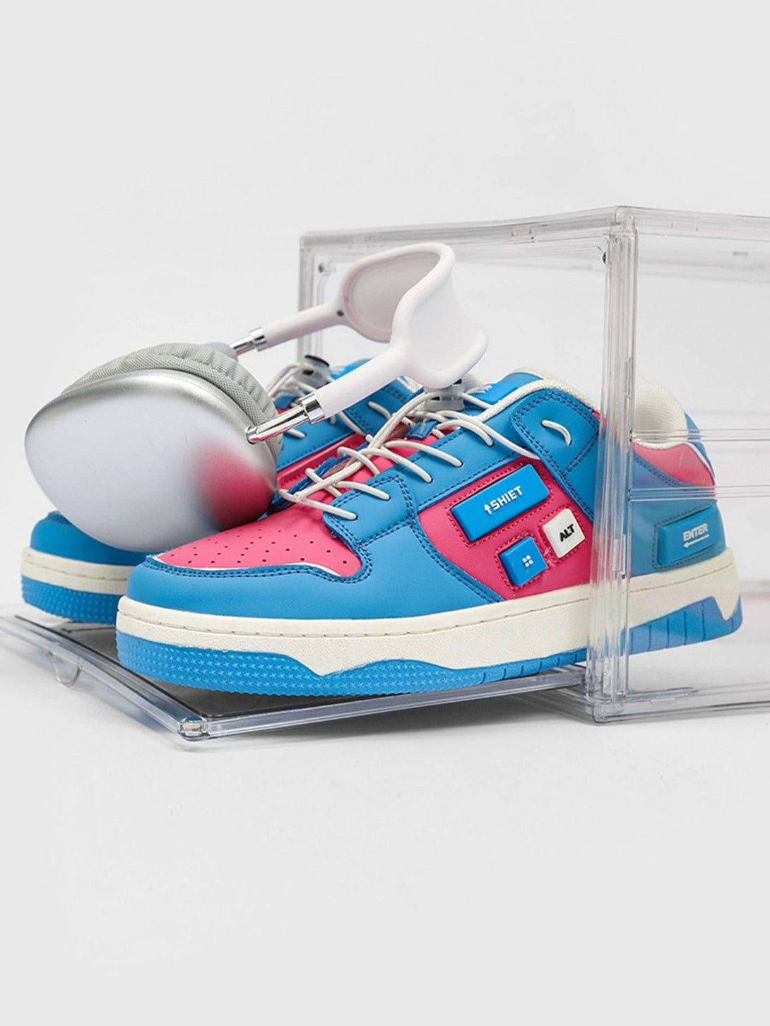 Front view of TALISHKO skate shoes in dodger blue and pink, paired with sleek headphones.