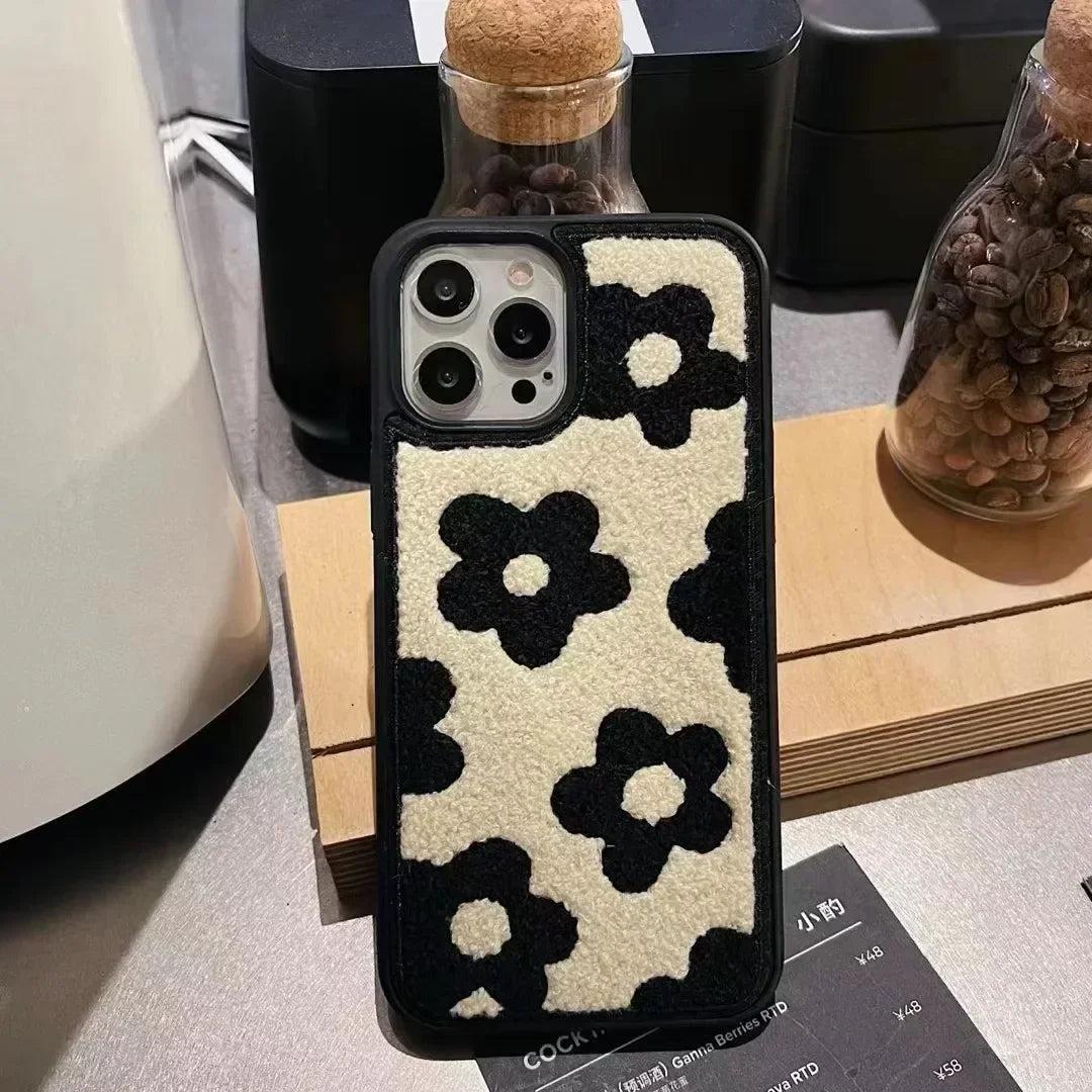TALISHKO iPhone case with plush black and white floral design, front view on a wooden surface.