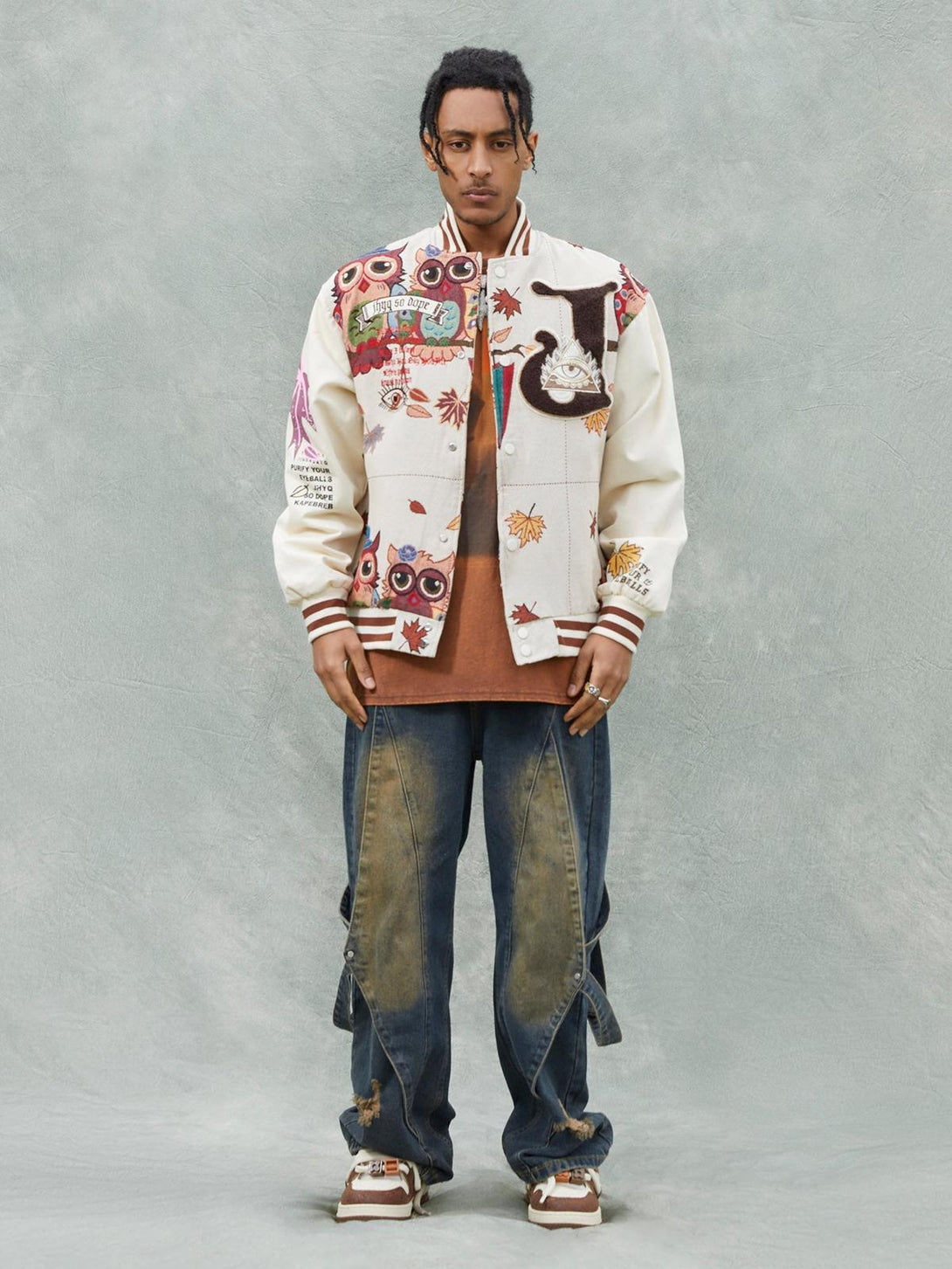 Model wearing a TALISHKO owl patch baseball jacket in beige, paired with baggy jeans.