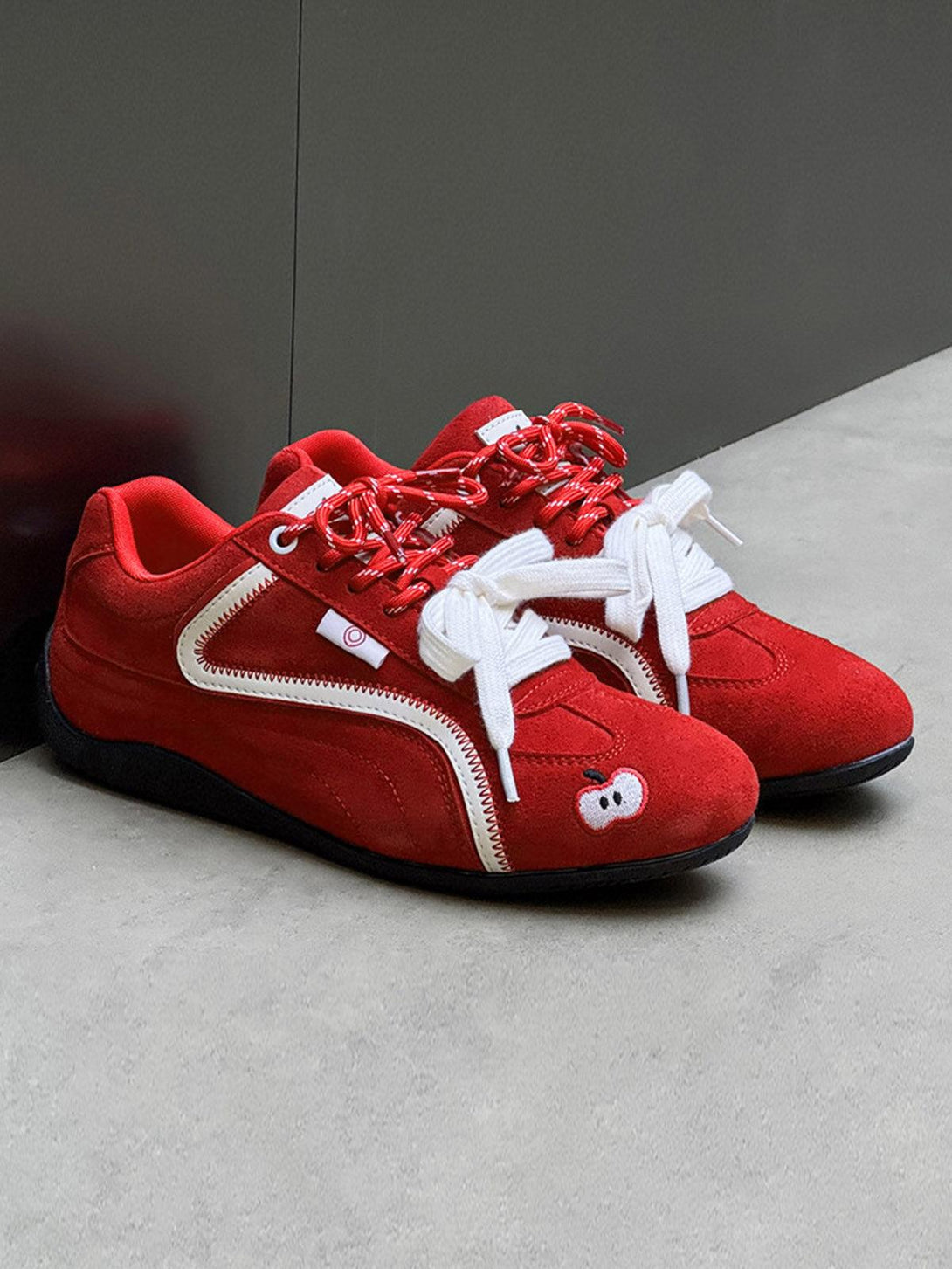 Red suede lace-up sneakers by TALISHKO, showcasing playful apple embroidery and bold street style.