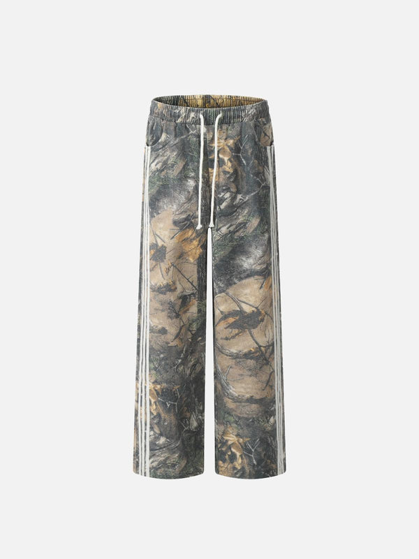 Front view of TALISHKO drapey pants in a tree branch digital print, featuring earthy green tones.