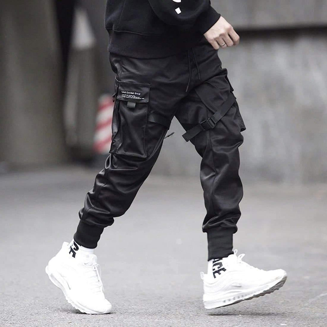 Model wearing TALISHKO tactical joggers with detailed straps, paired with white sneakers.